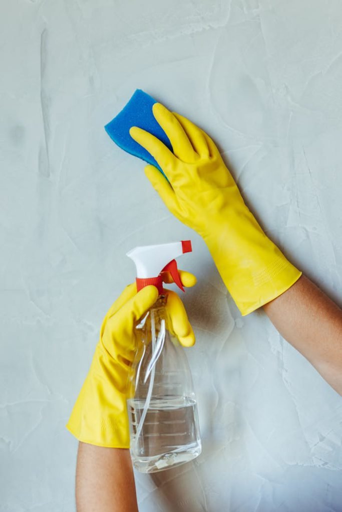 pexels-photo-28576635 Hands in yellow gloves cleaning wall with sponge and spray bottle.